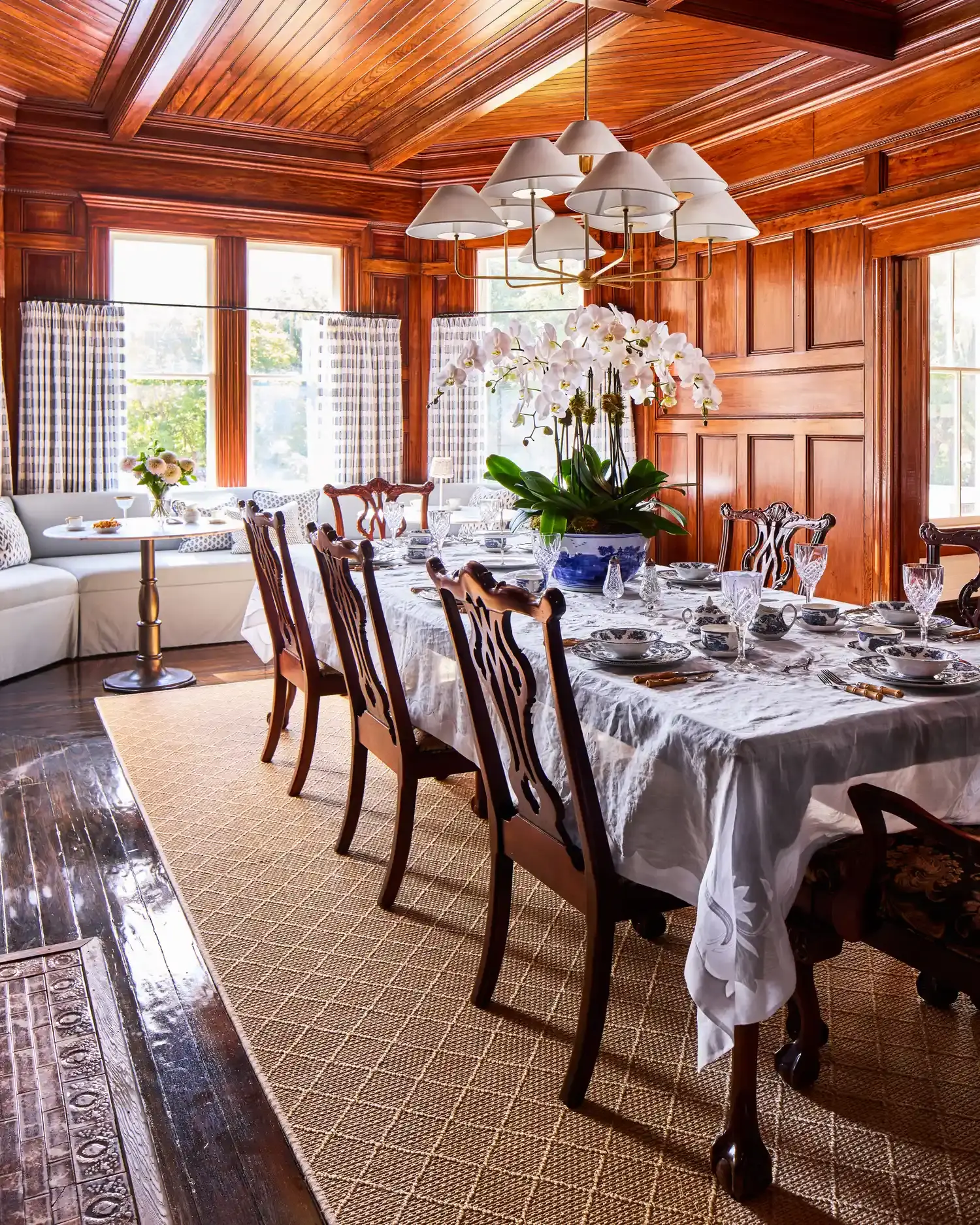 The paneled dining room with a coffered wooden ceiling, laid for dinner, water visible through the windows.